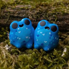 two little blue birds with hearts on them sitting in the grass next to a log