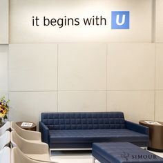 a blue couch sitting in front of a sign that says it begins with u on the wall