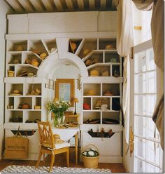 a room filled with lots of white shelves and wooden chairs next to a table in front of a mirror