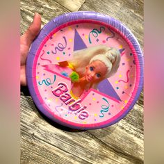 a hand holding a pink and purple paper plate with a barbie doll on it's face