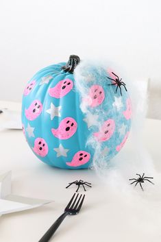 a blue pumpkin decorated with pink pigs and stars on it, sitting next to a fork