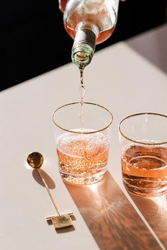 someone pouring water into two glasses with spoons