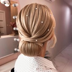 a woman with blonde hair in a ponytail and pearls on her head is seen from the back