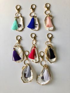 six different colored tassels hanging from gold hooks on a white surface, with one in the middle