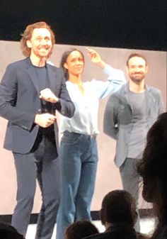 two men and a woman are standing on stage with their arms in the air as one man holds his hand up