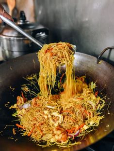 someone is stirring noodles in a wok on the stove