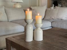 two candles sitting on top of a wooden table in front of a couch and chair