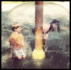 two children are playing in the water near a fire hydrant that is turned upside down