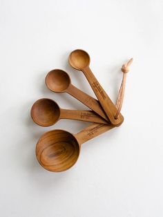 six wooden spoons are lined up on a white surface, one is empty and the other has five in it