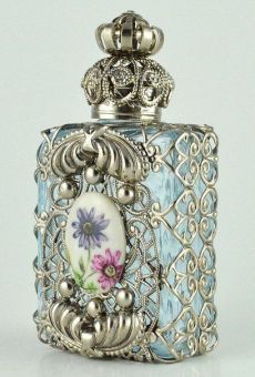 an ornate silver and blue glass flask with a flower decoration on the front, sitting on a white surface