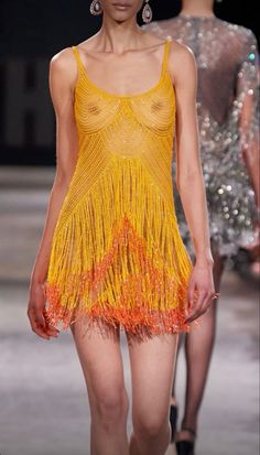 a model walks down the runway in a yellow dress with orange fringes on it