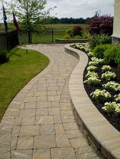 a brick walkway in front of a house with white flowers on the side and green grass around it