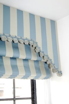 a blue and white striped roman blind with tassels on the top, in front of a window