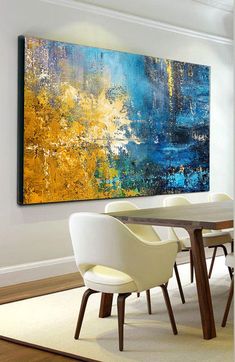 a dining room table with white chairs and a large painting on the wall