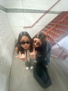 two young women standing in front of a staircase making the peace sign with their hands