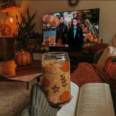 a person is holding an open book in front of a television and pumpkins on the couch