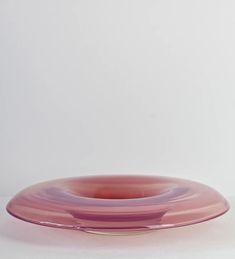 a pink glass plate sitting on top of a white table next to a red vase