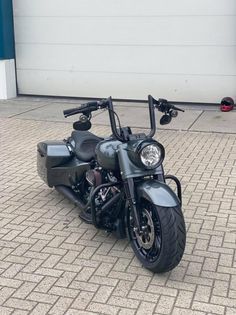 a black motorcycle parked on top of a brick road next to a white garage door