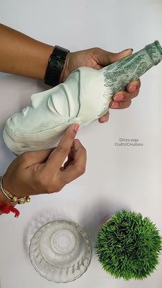 two hands holding an object over a table next to a potted plant and glass plate