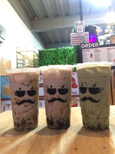 three iced drinks with mustaches on them sitting on top of a wooden table in a store