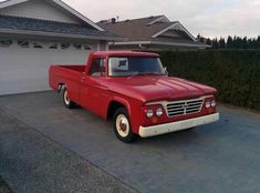 an old red pickup truck parked in front of a house with a garage door open