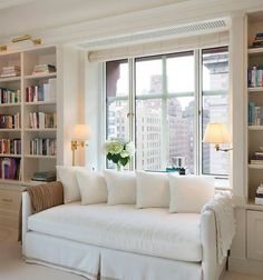 a white couch sitting in front of a window next to a book shelf filled with books