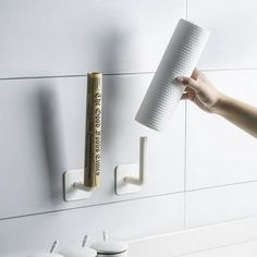 a person holding a roll of toilet paper in front of a wall mounted toothbrush dispenser