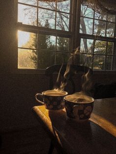 two coffee cups sitting on top of a wooden table in front of a large window