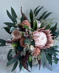 a vase filled with pink flowers and greenery on top of a white table cloth