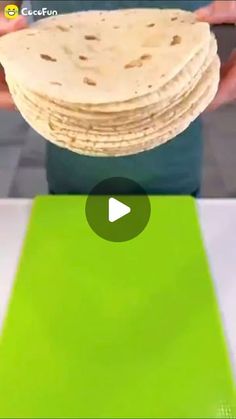 a stack of tortillas sitting on top of a green place mat next to a person's hand