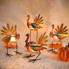 four metal flamingos sitting on top of a table next to pumpkins and candles