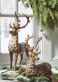 two deer figurines sitting next to each other in front of a window