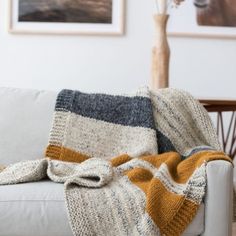 a white couch with a blanket on top of it next to a vase filled with flowers