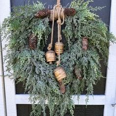 a wreath with pine cones and bells hanging on a door