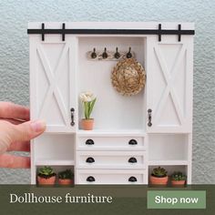 a hand is holding a miniature white cabinet with drawers and plants in it, which has a potted plant on the top shelf