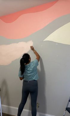 a woman painting a wall with pink and grey colors