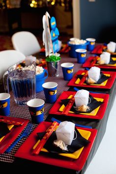 the table is set with red and blue plates, cups, and napkins on it