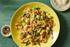 a yellow plate topped with pasta and asparagus on top of a green table