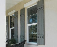 two windows with shutters on the side of a white building and a black chair