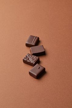 three pieces of chocolate sitting on top of a brown table next to one piece of chocolate