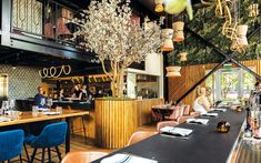 people are sitting at tables in a restaurant with blue chairs and wooden counter tops on either side of the bar