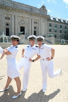 three women in white uniforms are posing for a photo on a brick walkway near a large building