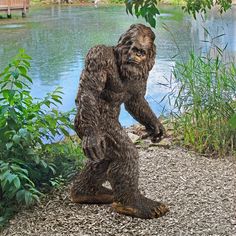 a statue of a bigfoot standing in front of a body of water and trees