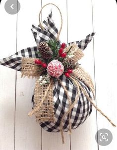 a christmas ornament hanging on the side of a white wooden wall with pine cones and berries