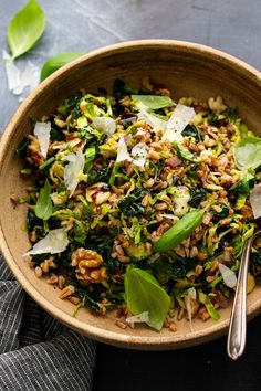 a bowl filled with greens and nuts on top of a table next to a spoon