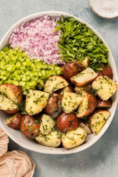 a white bowl filled with potatoes, green onions and red onion next to other ingredients