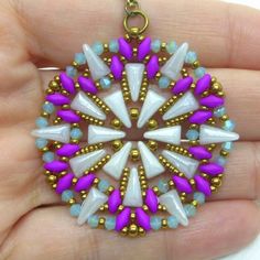 a hand holding a purple and white beaded pendant