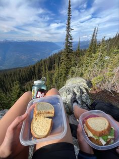 two people sitting on top of a mountain with sandwiches in plastic containers next to them