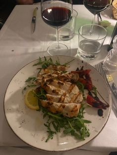 a white plate topped with meat and veggies next to glasses of red wine