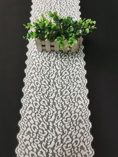 a plant is sitting on top of a white lace table runner with black and white designs